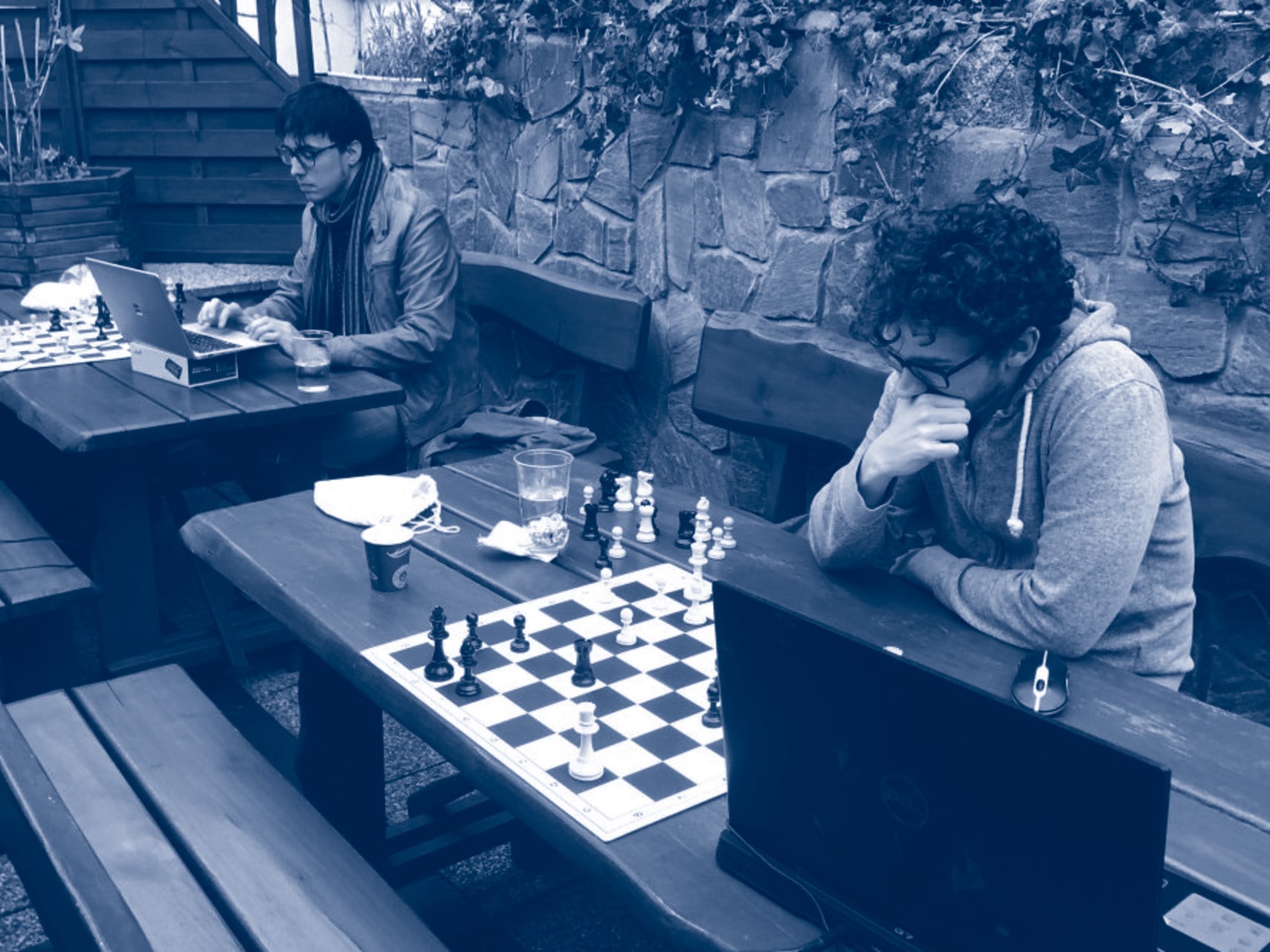 People playing hybrid chess with a physical chessboard and a laptop